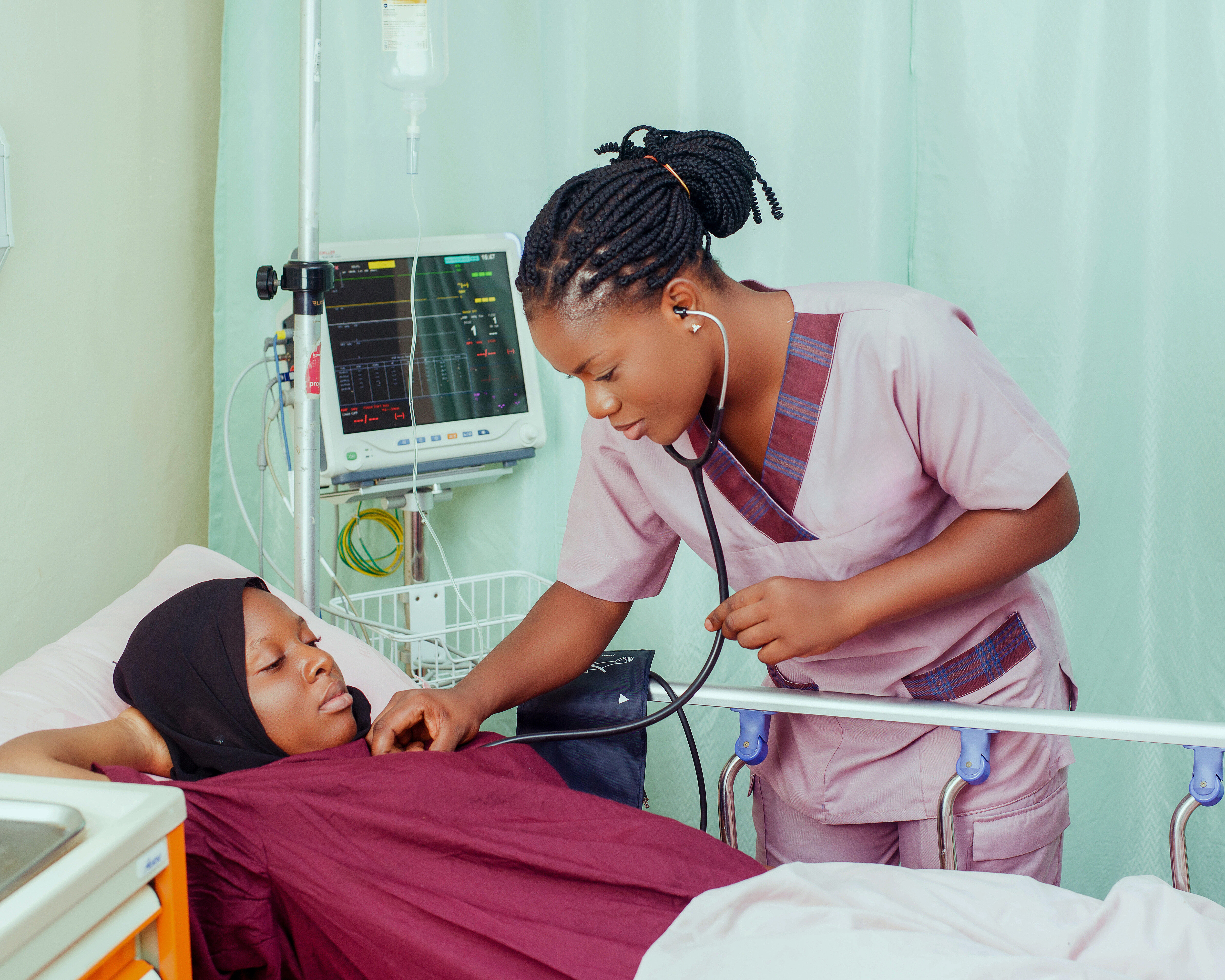 Young nurse examines a patient by the bed side with a stethoscope.